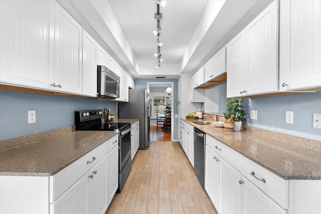 kitchen featuring stainless steel appliances, a tray ceiling, light wood-style flooring, and white cabinetry