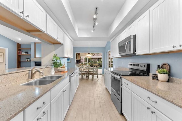 kitchen with a sink, white cabinets, light wood-style floors, appliances with stainless steel finishes, and a raised ceiling