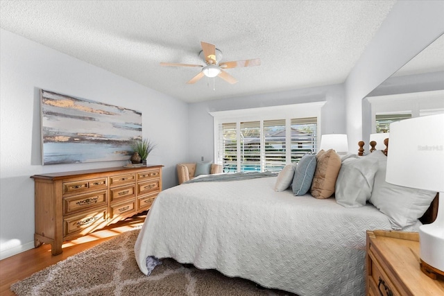 bedroom featuring a ceiling fan, a textured ceiling, baseboards, and wood finished floors