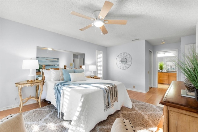 bedroom featuring ceiling fan, a textured ceiling, light wood-style flooring, visible vents, and baseboards