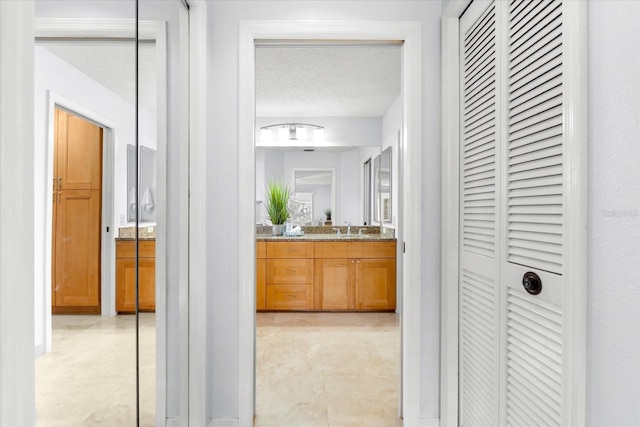 corridor featuring a textured ceiling, a sink, and light tile patterned flooring