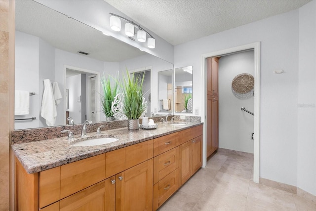 full bath featuring double vanity, a textured ceiling, visible vents, and a sink