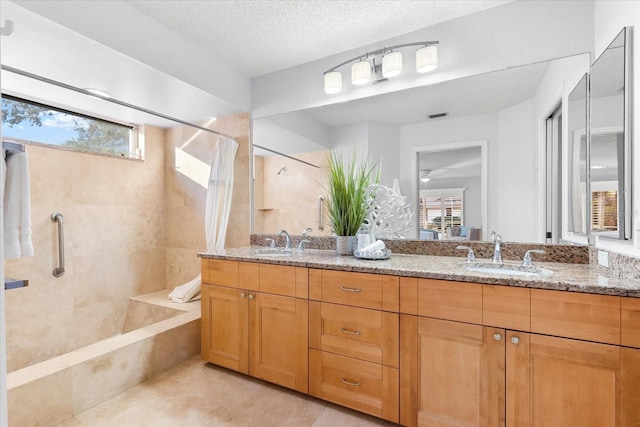 bathroom featuring tiled shower, a sink, a textured ceiling, and double vanity