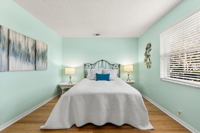 bedroom with baseboards, a textured ceiling, visible vents, and wood finished floors