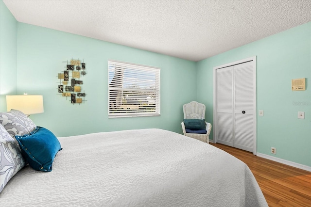 bedroom featuring a closet, a textured ceiling, baseboards, and wood finished floors