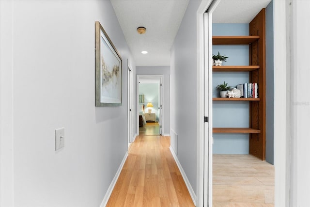 corridor featuring a textured ceiling, light wood finished floors, built in shelves, and baseboards