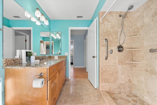 bathroom featuring a textured ceiling, vanity, visible vents, baseboards, and a tile shower