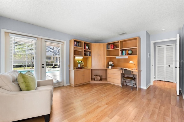 home office with light wood finished floors, built in desk, a textured ceiling, and visible vents