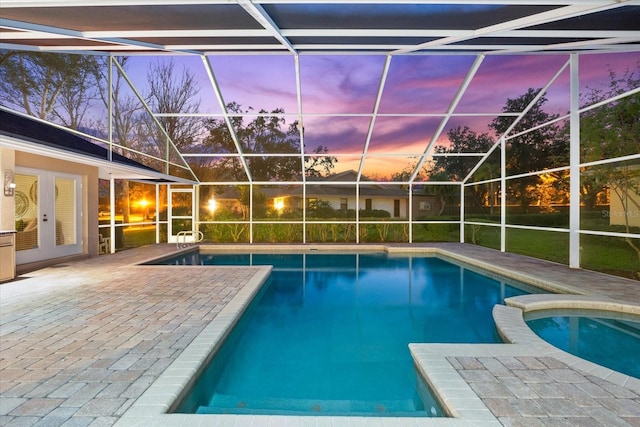 pool at dusk with a pool with connected hot tub, french doors, glass enclosure, and a patio