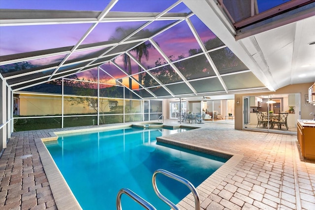 pool at dusk featuring outdoor dining area, a patio, a pool with connected hot tub, a sink, and a lanai