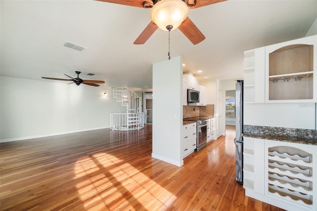 kitchen featuring white cabinetry, wood-type flooring, ceiling fan, stainless steel appliances, and backsplash