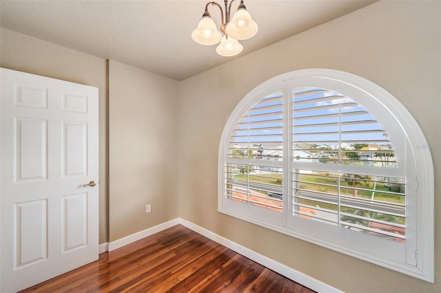 spare room with dark hardwood / wood-style floors and a chandelier