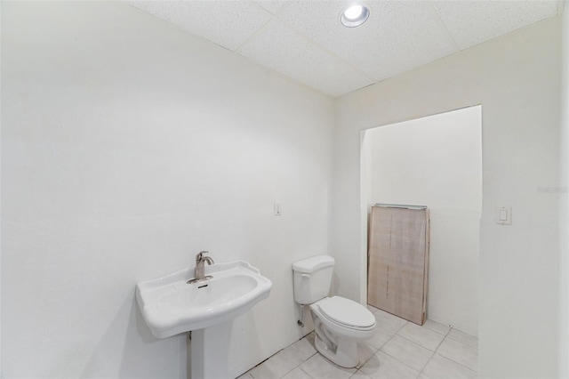 bathroom with a paneled ceiling, tile patterned floors, toilet, and sink