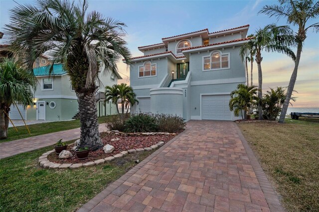 6423 Driftwood Dr, Hudson, FL 34667 - mediterranean / spanish home with decorative driveway, stucco siding, a garage, a tiled roof, and a front lawn