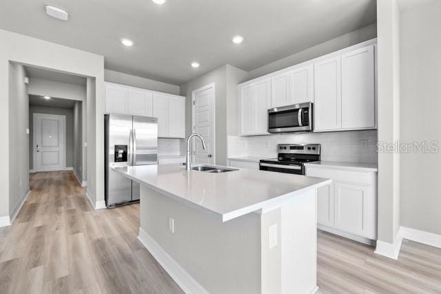 kitchen with appliances with stainless steel finishes, light wood-type flooring, sink, a center island with sink, and white cabinetry