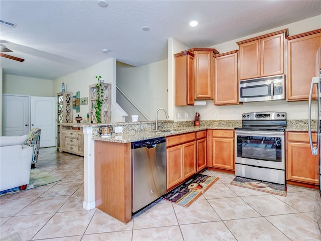 kitchen with ceiling fan, kitchen peninsula, sink, light stone countertops, and appliances with stainless steel finishes