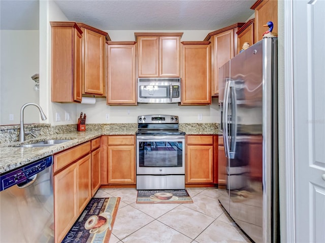 kitchen with a textured ceiling, stainless steel appliances, sink, light tile patterned flooring, and light stone counters