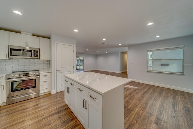 kitchen with a center island, white cabinets, decorative backsplash, light stone countertops, and stainless steel appliances