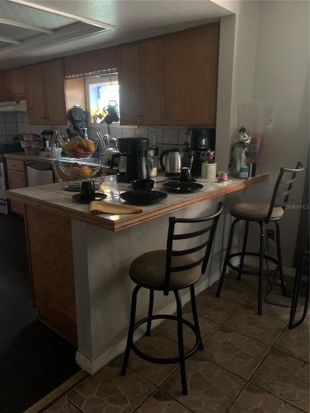 kitchen featuring stainless steel dishwasher, kitchen peninsula, a breakfast bar area, and exhaust hood