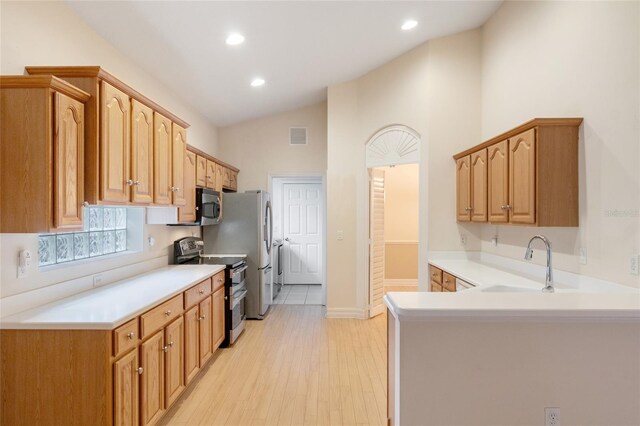 kitchen featuring lofted ceiling, kitchen peninsula, sink, light hardwood / wood-style flooring, and appliances with stainless steel finishes