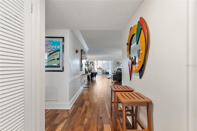 corridor featuring dark wood-type flooring, a textured ceiling, and ornamental molding