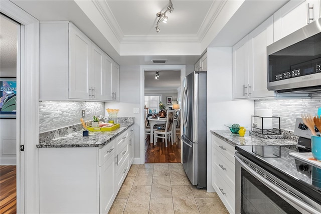 kitchen featuring rail lighting, stainless steel appliances, dark stone countertops, ornamental molding, and white cabinets