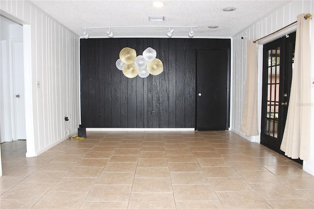 tiled spare room featuring wood walls, french doors, and rail lighting