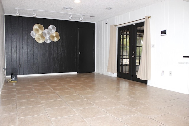 spare room featuring a textured ceiling, wood walls, french doors, and track lighting