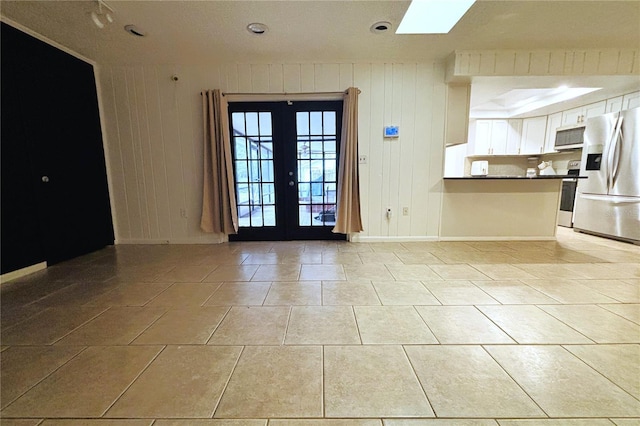 unfurnished room featuring a skylight, wooden walls, french doors, and light tile patterned flooring