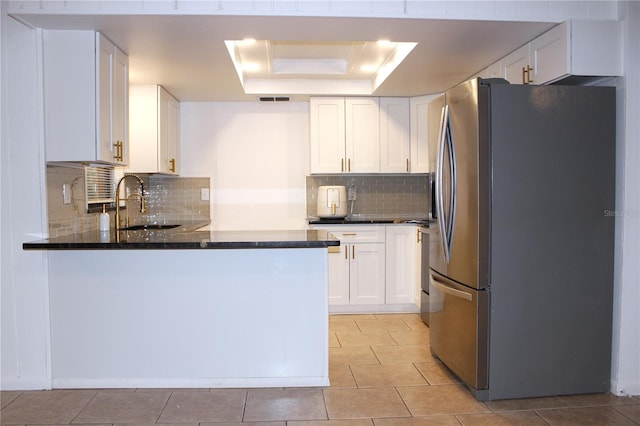 kitchen featuring stainless steel refrigerator, white cabinetry, sink, a raised ceiling, and tasteful backsplash