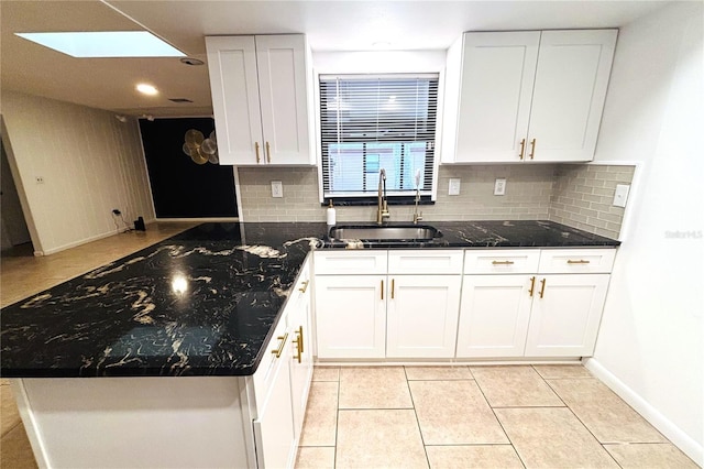 kitchen with a skylight, sink, white cabinets, and dark stone counters