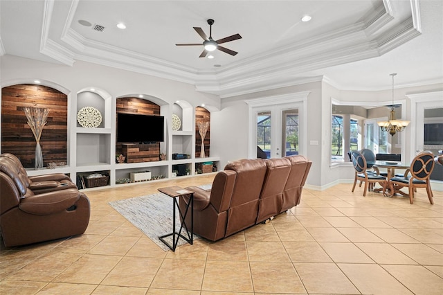 living room with light tile patterned floors, a tray ceiling, ceiling fan with notable chandelier, built in features, and ornamental molding