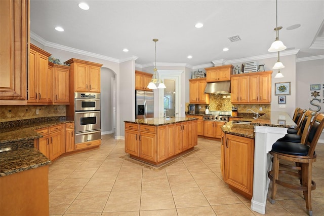 kitchen with a center island, hanging light fixtures, stainless steel appliances, dark stone countertops, and ventilation hood