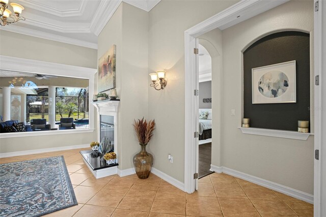 entrance foyer with ceiling fan with notable chandelier, a raised ceiling, ornamental molding, and light tile patterned floors