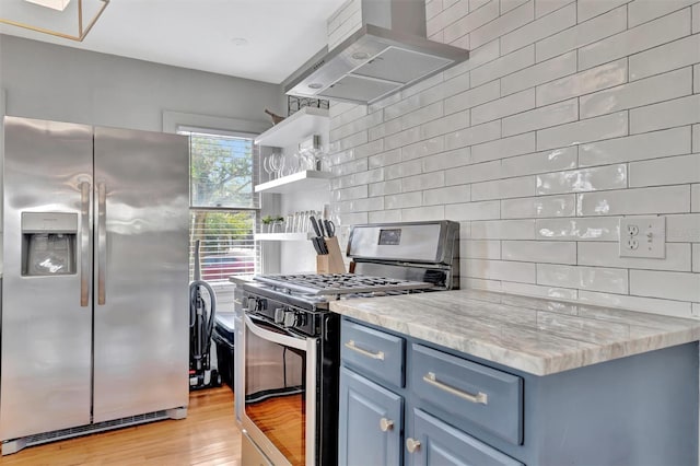 kitchen featuring wall chimney exhaust hood, stainless steel appliances, tasteful backsplash, light hardwood / wood-style flooring, and blue cabinets