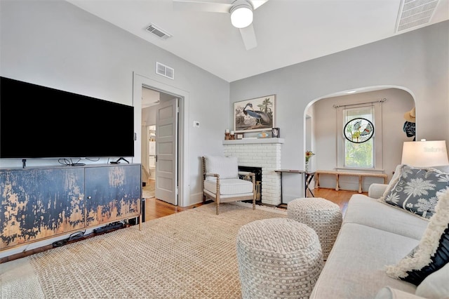 living room with light hardwood / wood-style floors, a brick fireplace, and ceiling fan