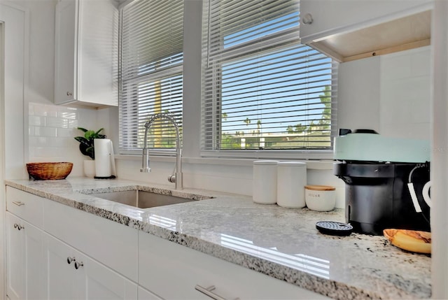 kitchen featuring white cabinets, backsplash, light stone counters, and sink