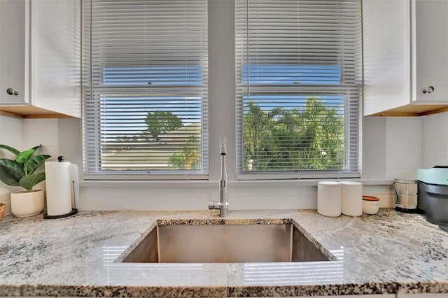 kitchen featuring light stone counters, white cabinetry, and sink