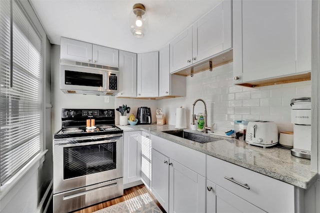 kitchen with stainless steel electric stove, white cabinets, sink, light hardwood / wood-style floors, and light stone counters