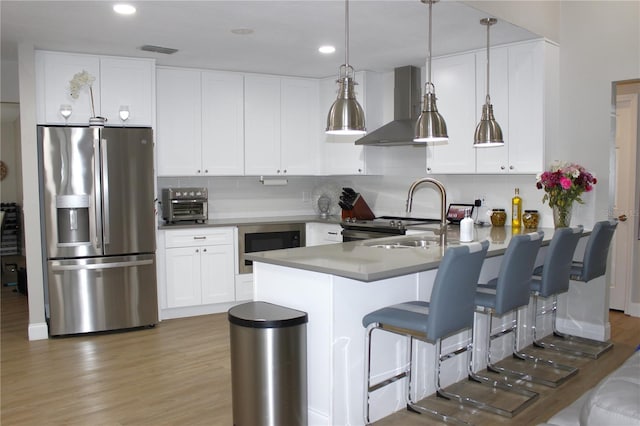 kitchen with white cabinetry, wall chimney range hood, hanging light fixtures, stainless steel fridge, and kitchen peninsula