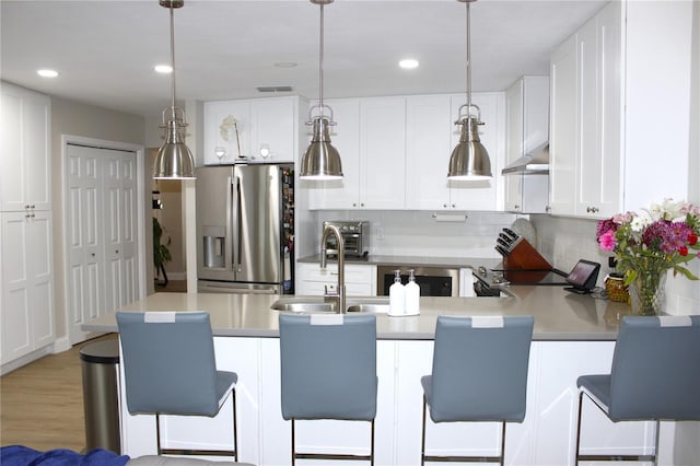 kitchen with white cabinets, pendant lighting, stainless steel fridge, and a breakfast bar area