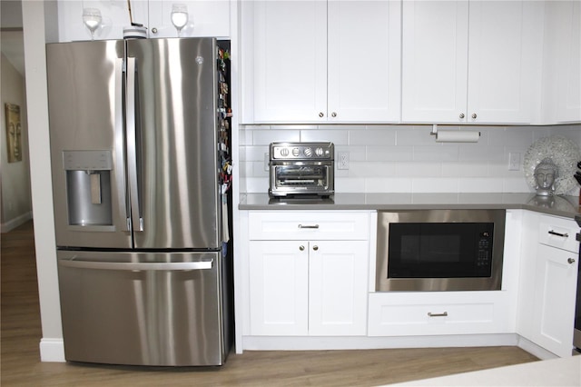 kitchen featuring white cabinetry, stainless steel refrigerator with ice dispenser, tasteful backsplash, built in microwave, and light hardwood / wood-style flooring