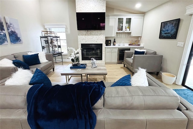 living room with vaulted ceiling, light wood-type flooring, beverage cooler, and a tile fireplace