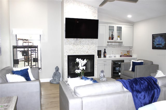 living room with ceiling fan, vaulted ceiling, a fireplace, light wood-type flooring, and beverage cooler