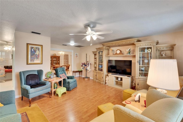 living room featuring ceiling fan with notable chandelier, a textured ceiling, and light hardwood / wood-style floors