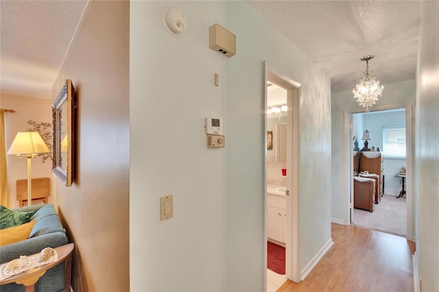 hallway featuring a textured ceiling, a chandelier, and light hardwood / wood-style floors