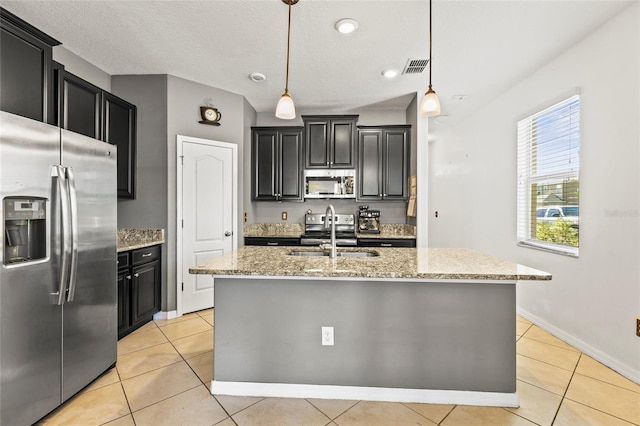 kitchen with a center island with sink, appliances with stainless steel finishes, hanging light fixtures, light tile patterned floors, and sink