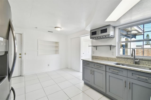 kitchen featuring stainless steel fridge, a skylight, gray cabinetry, and sink