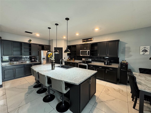 kitchen with decorative light fixtures, tasteful backsplash, sink, an island with sink, and stainless steel appliances