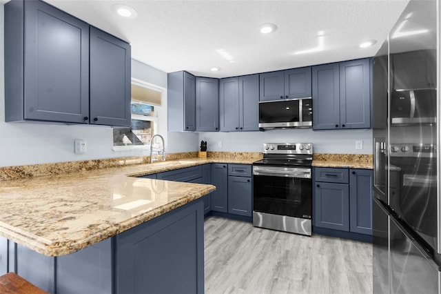 kitchen featuring kitchen peninsula, sink, light wood-type flooring, light stone countertops, and stainless steel appliances